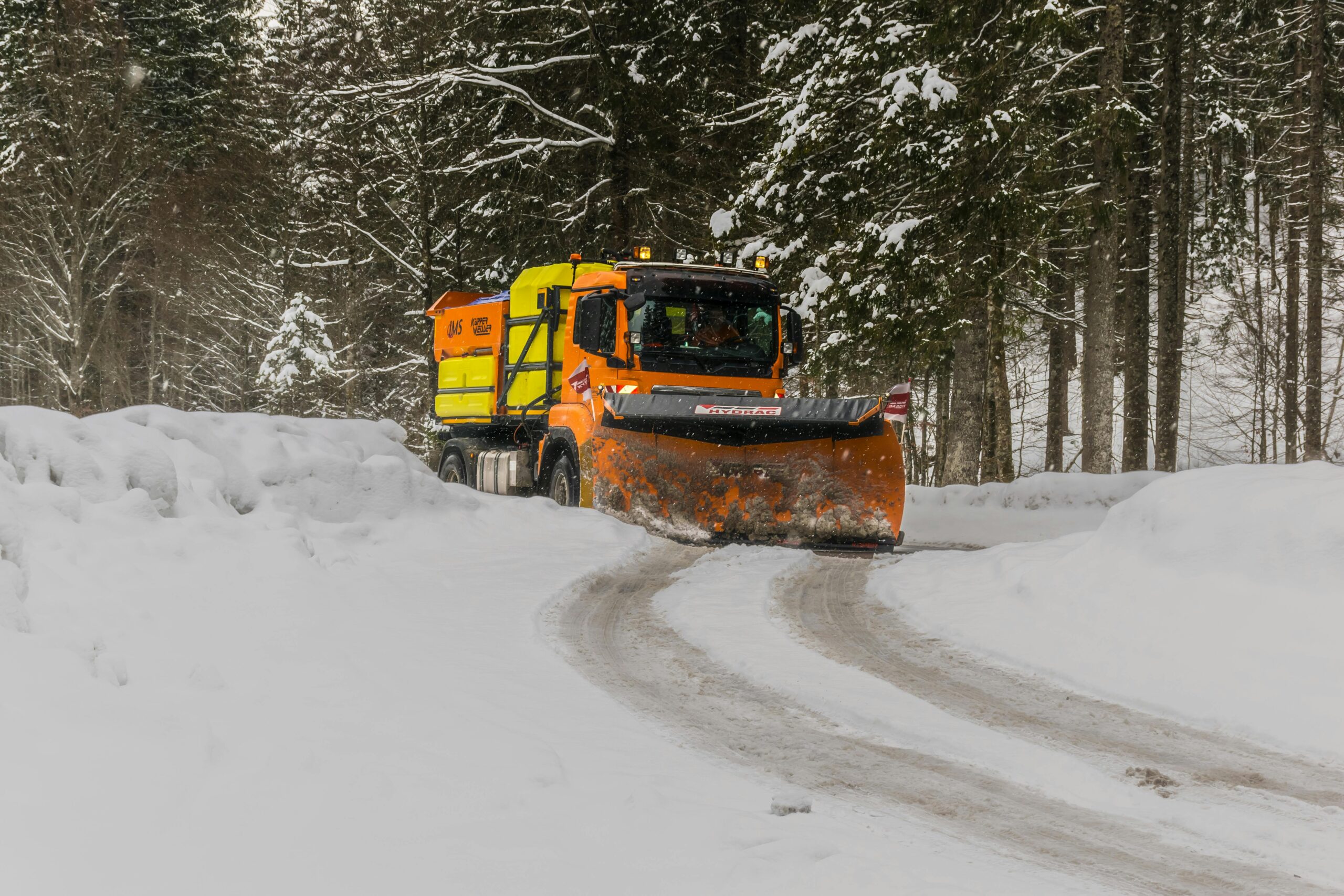A snow plow clearing a snow-laden road through a forest in Ettal, Germany.